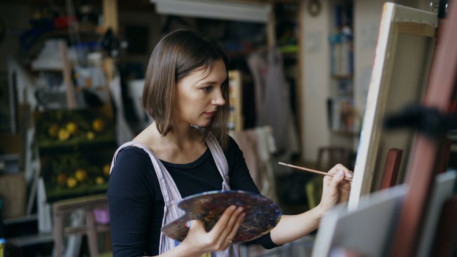 Female artist painting with focus in an art studio, holding a palette.