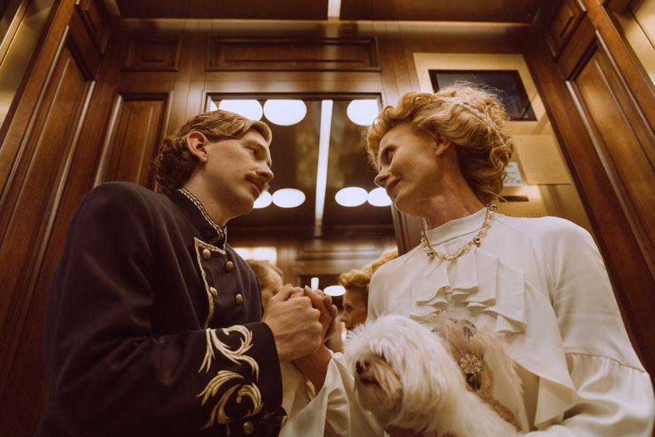 Charming couple holding hands with a Maltese dog in a vintage elevator setting.