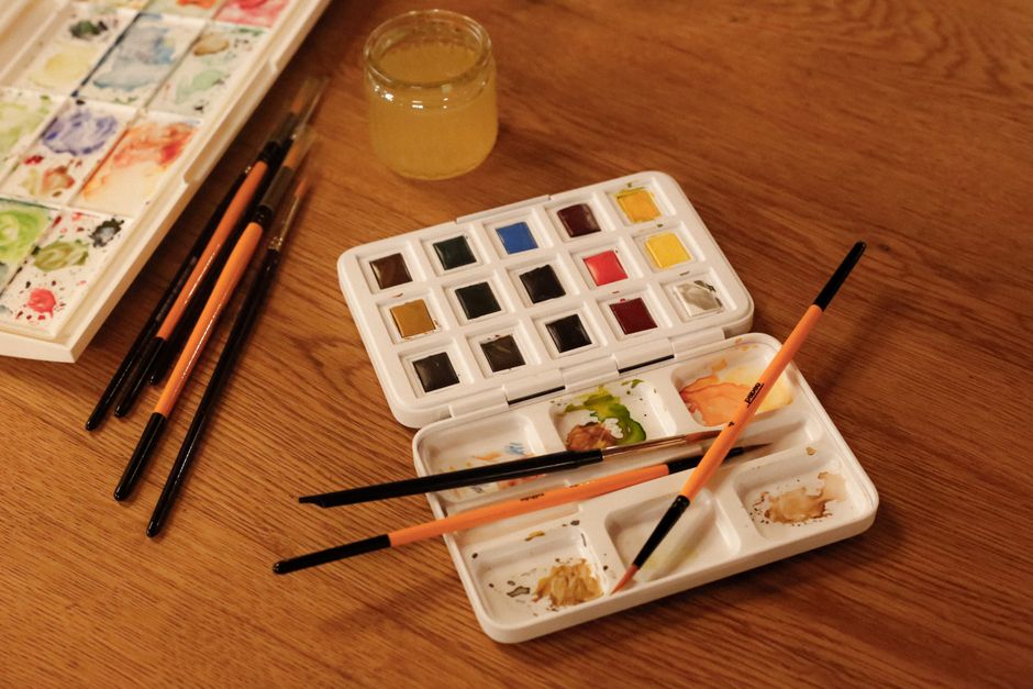A creative arrangement of watercolor paints, brushes, and water jar on a table.